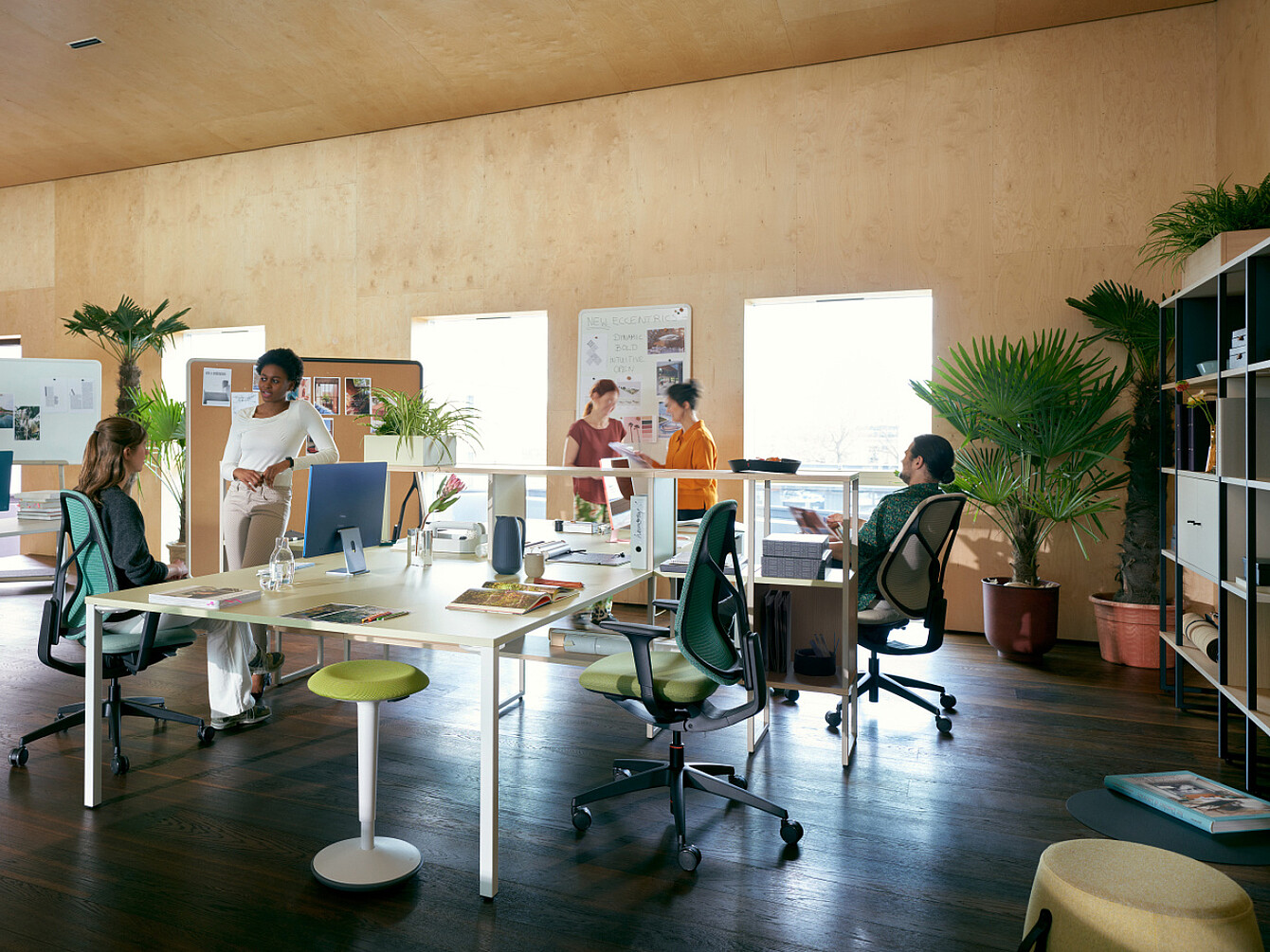 Uffici open space con luce naturale, piante, sedie ergonomiche e dipendenti che collaborano, riflettendo un ambiente di lavoro incentrato sul benessere e sul supporto olistico.