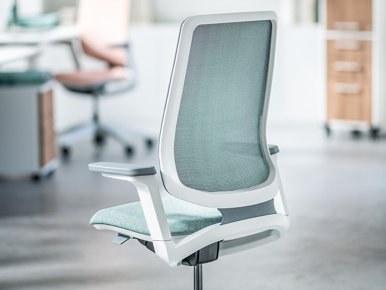 Light green ergonomic office chair with mesh backrest and white frame in a modern office setting