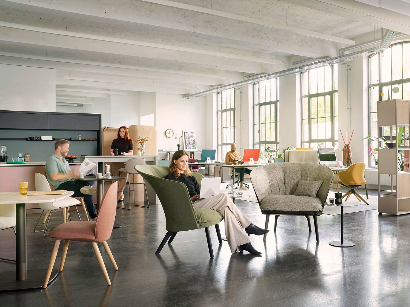 Open workspace with several people sitting at tables and armchairs in a bright room with large windows and exposed ceiling beams