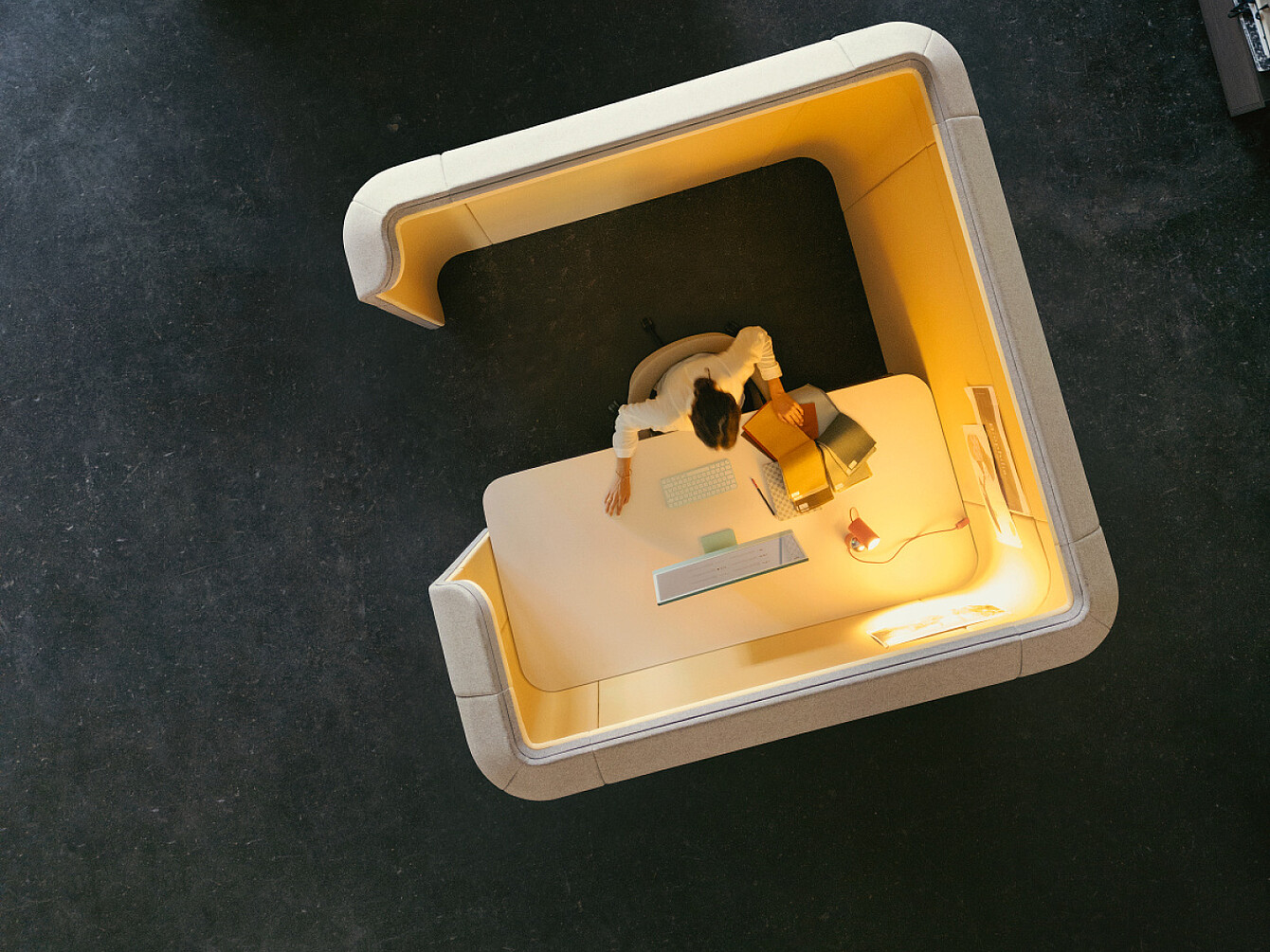 Overhead view of a person working in a specialized, enclosed workspace with cushioned walls and integrated lighting, supporting focused work in an evolving office environment.
