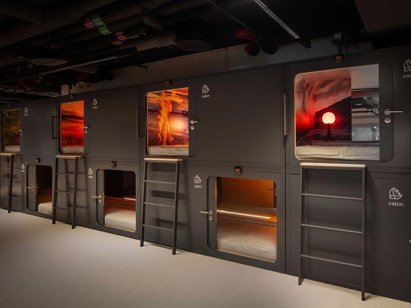 Stacked black sleeping pods with ladders and doors, each pod featuring a window showing a volcanic eruption scene.