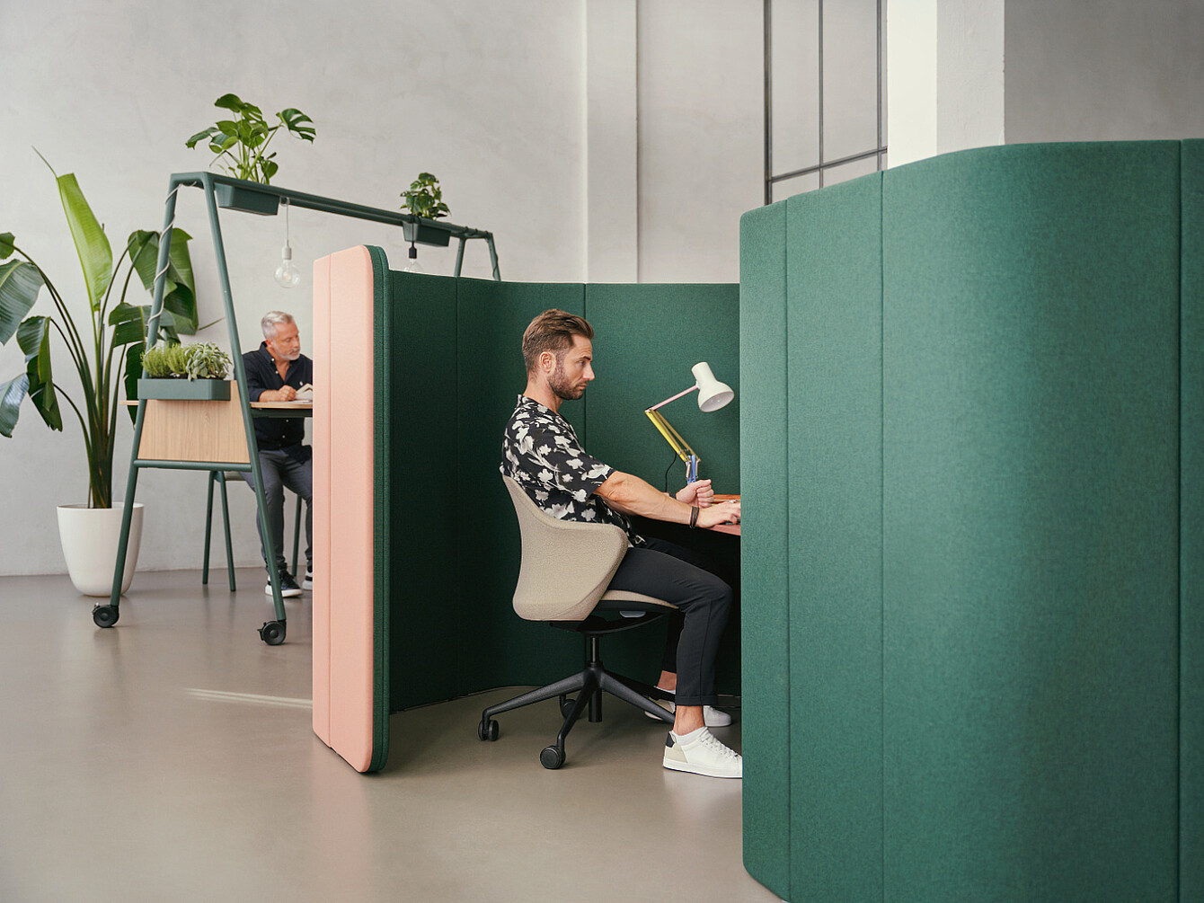 Uomo che lavora in una cabina acustica verde in un ufficio moderno con luce naturale e piante, a testimonianza delle priorità in materia di benessere sul posto di lavoro.