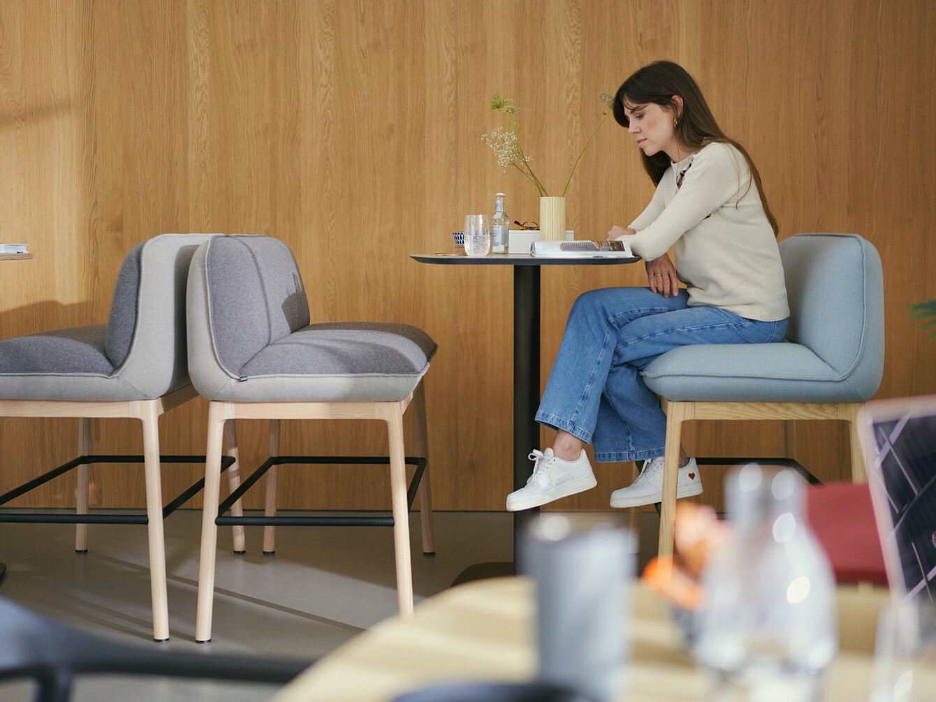 Donna seduta da sola a un tavolino in una moderna sala relax con pareti in legno, intenta a leggere o a lavorare in silenzio, che illustra un ambiente tranquillo e favorevole al benessere dei dipendenti.