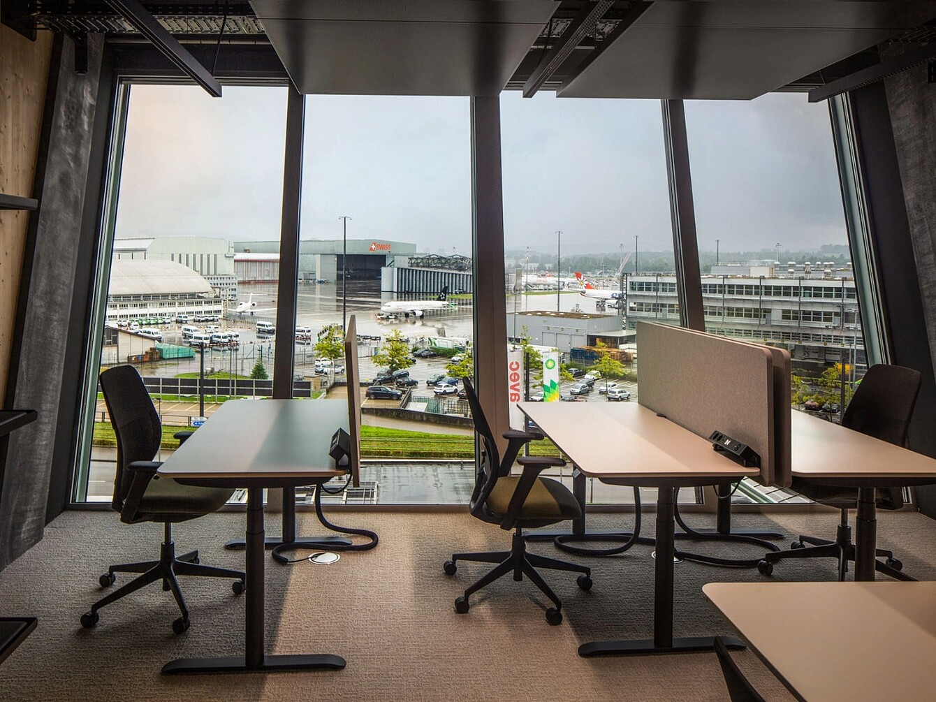 Office workspace with Sedus chairs and desks facing large windows overlooking Zurich Airport and parked airplanes.