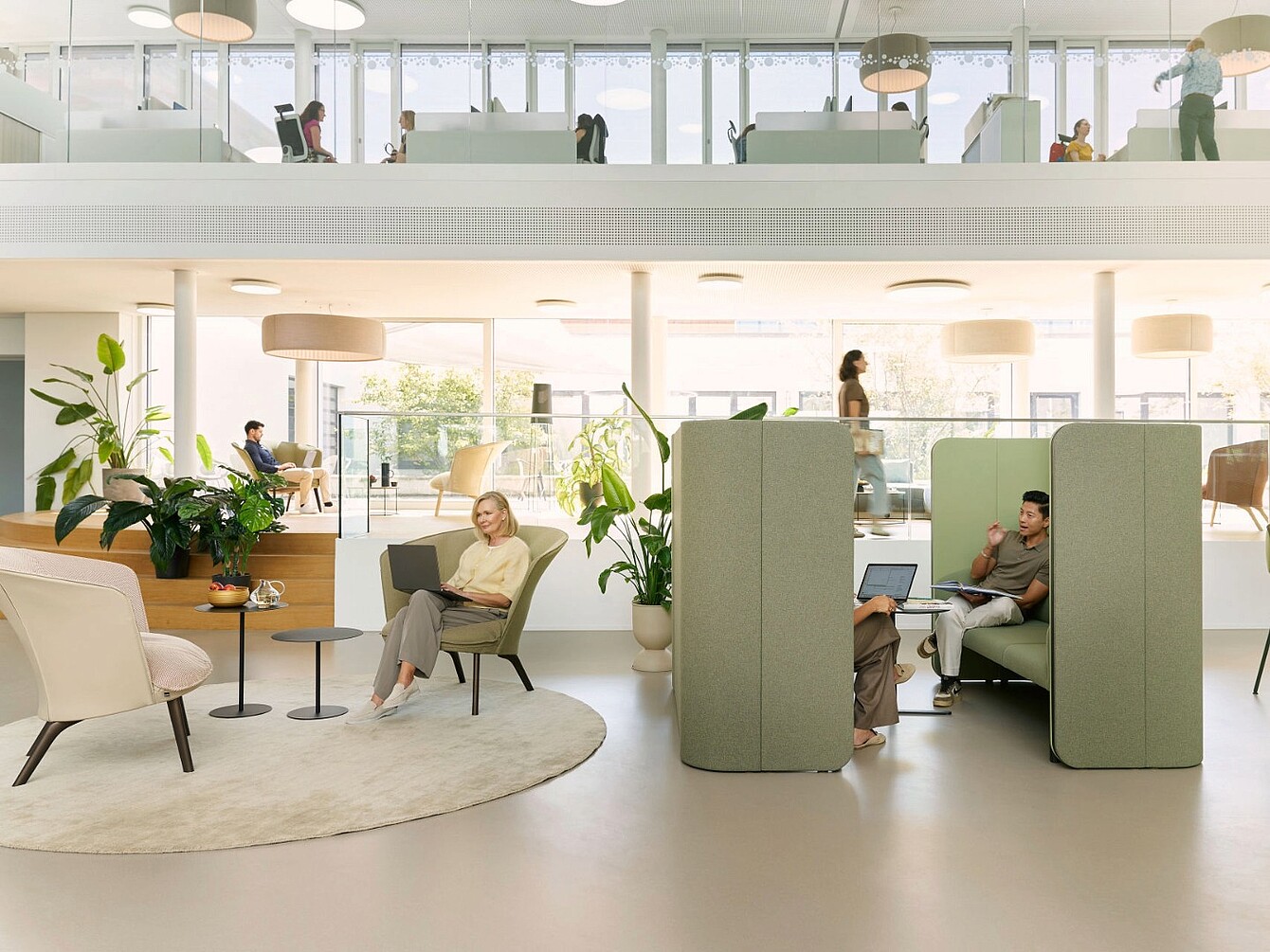 Modern office space with open seating, high-backed acoustic booths, and natural light from large windows