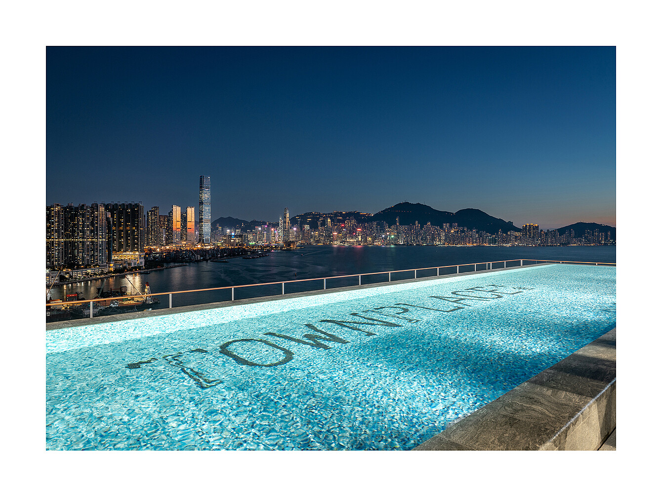 Piscina a sfioro sul tetto con la scritta "TOMMY LIFE" visibile sul fondo della piscina che si affaccia sullo skyline della città al tramonto
