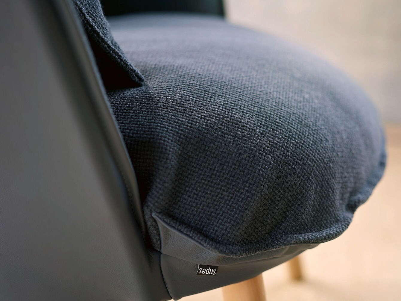 Primer plano del asiento de una se:cove silla con tapizado texturizado y una pequeña etiqueta de tela que muestra la marca Sedus