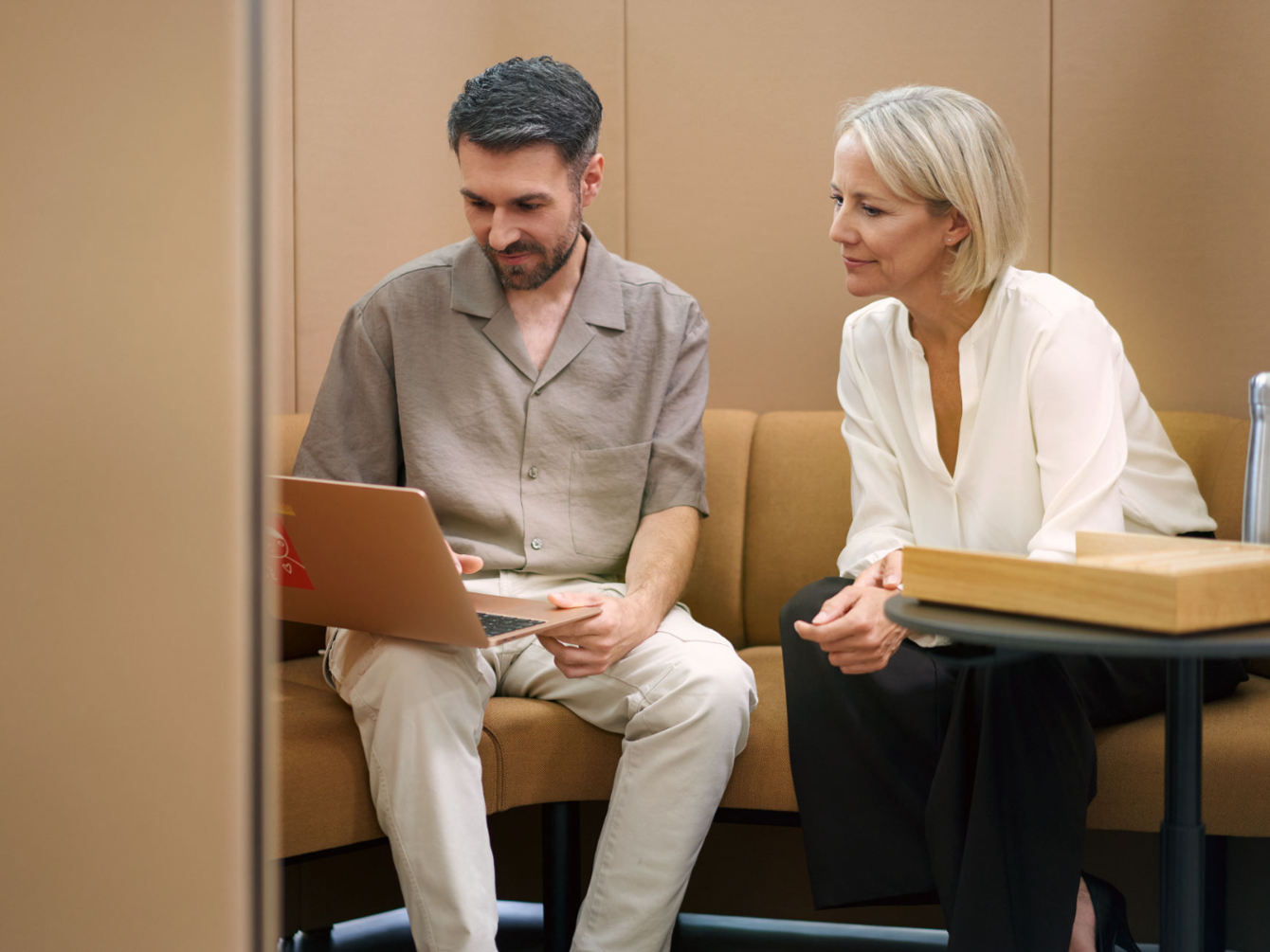 Two people sitting side by side on a brown couch looking at a laptop